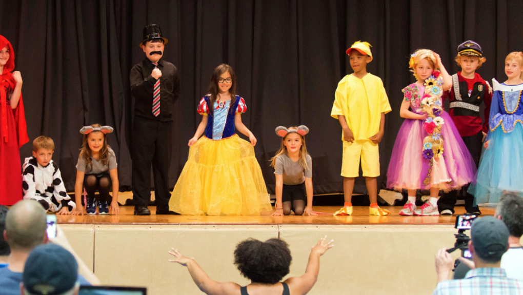 Children dressed as fairy tale characters line up across a stage